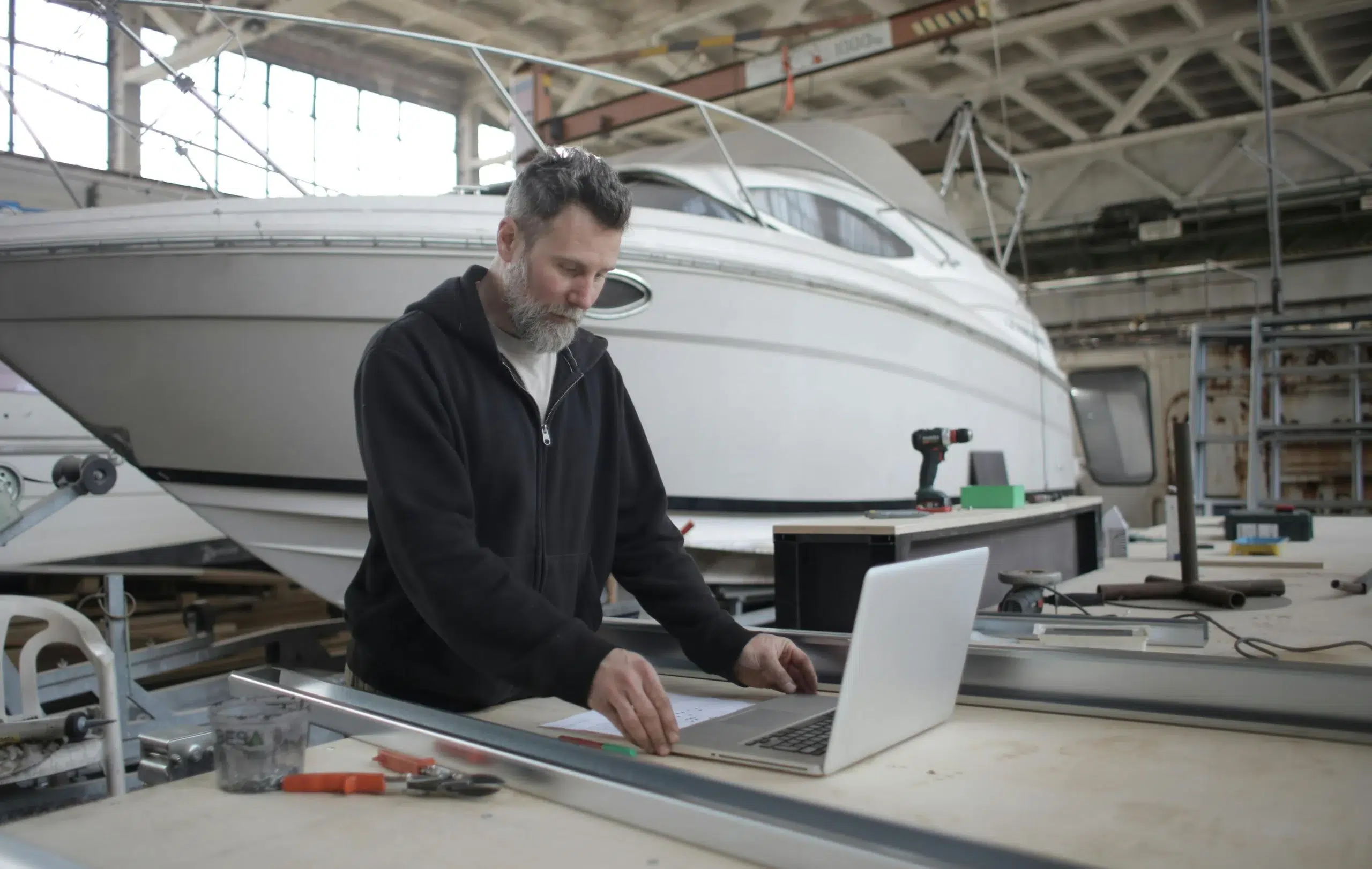 An industrial maintenance manager using a laptop to coordinate multi-site asset lifecycle management in a large-scale manufacturing and transport facility.