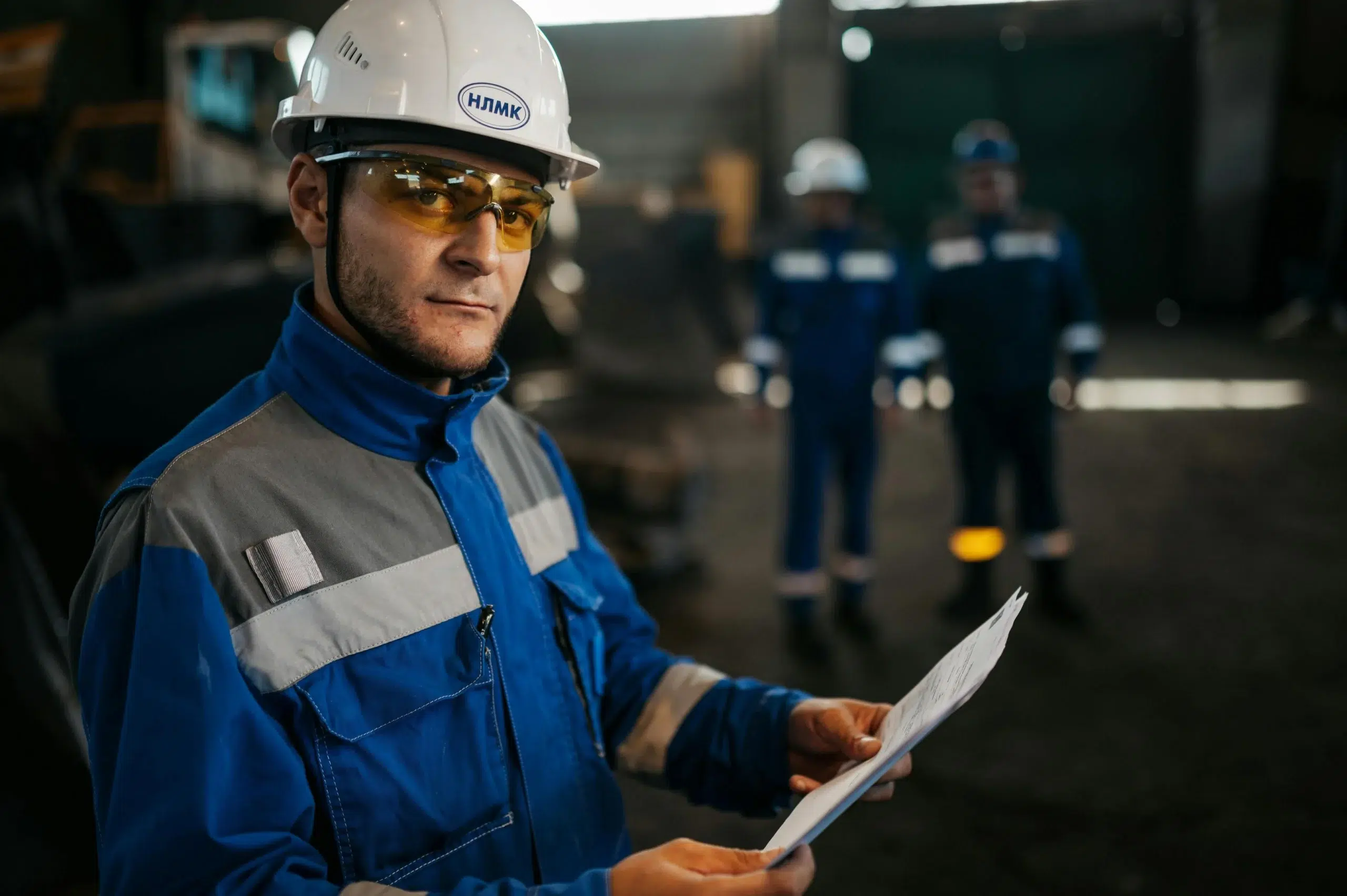 A maintenance technician in a white hard hat and blue uniform reviewing a paper log, illustrating the manual processes many manufacturing teams use before adopting a CMMS.