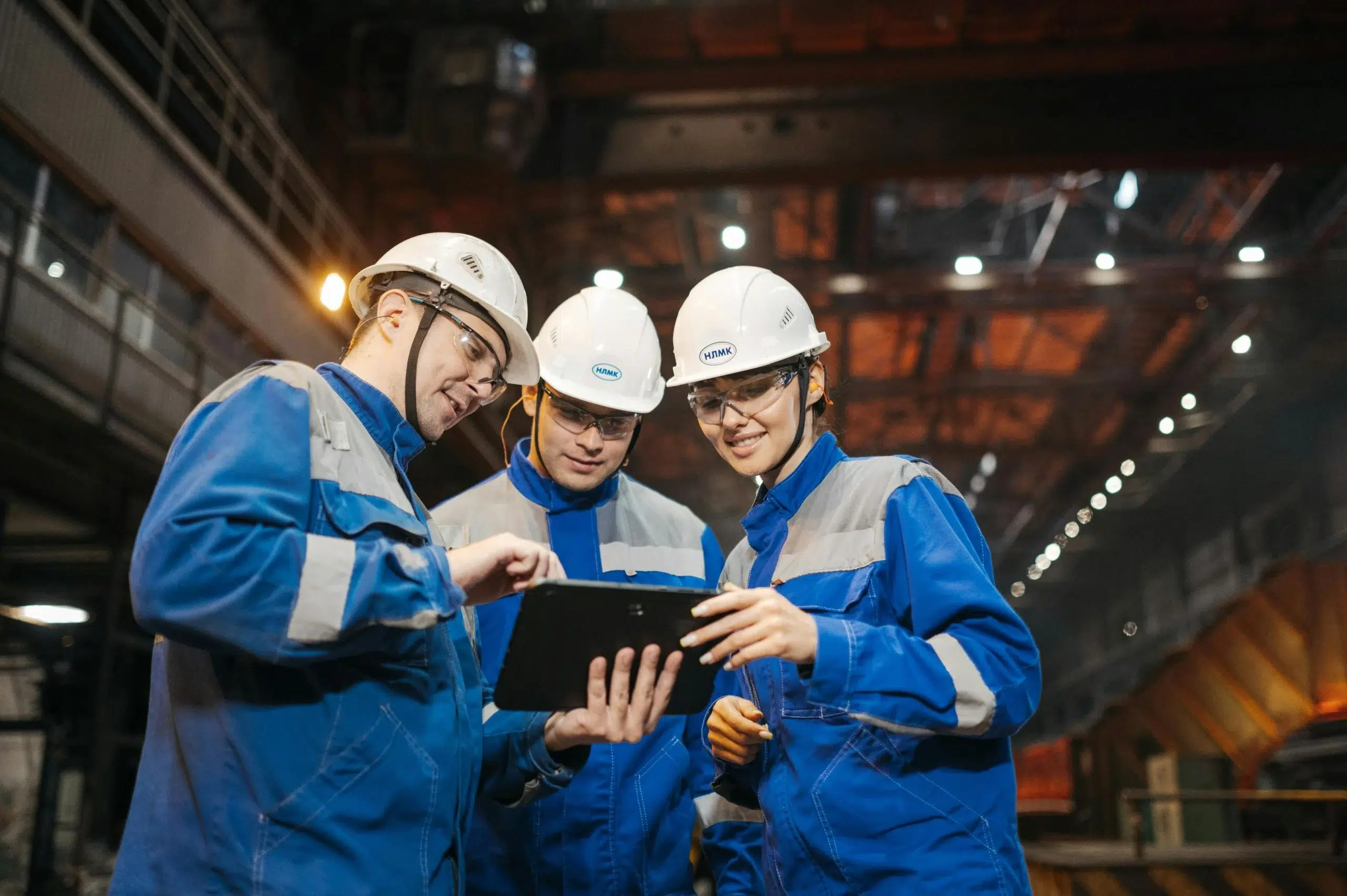 Three technicians in an industrial setting using a tablet to access mobile CMMS features, allowing them to log maintenance activities directly where the work happens.